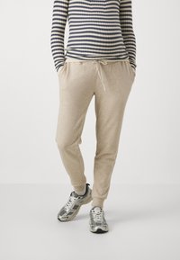 Beige joggebukser med snøring i livet og sidelommer, paret med grå trening sneakers og en marineblå og kremfarget stripete topp.