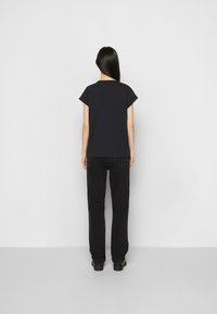 Svart kortärmad t-shirt, avslappnad passform, matchad med högmidjade svarta jeans och klumpiga svarta skor, sedd bakifrån.