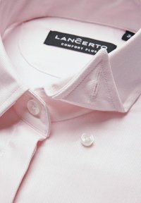 Jasnoróżowa bawełniana koszula z kołnierzykiem typu point, z zapięciem na guziki i subtelną teksturą. Metka mówi "Lancerto Comfort Plus."