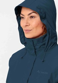 Giacca impermeabile blu navy con cappuccio regolabile, alto colletto e zip frontale. Presenta logo e dettagli con cordino per un miglior fitting.