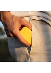 Geel draagbaar apparaat dat gedeeltelijk in een lichtgekleurde stoffen zak zit, met een gladde textuur en de tekst "Citrus Noon" op het oppervlak.