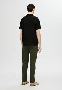 Czarna koszulka polo z krótkim rękawem, żebrowana, zestawiona z oliwkowymi spodniami, prosty krój, widoczne szwy i casualowe obuwie.