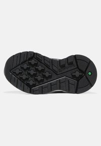 Black rubber outsole with a textured surface. Features deep grooves and hexagonal patterns for traction. White midsole with green accent.