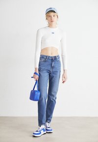 Top corto blanco acanalado, jeans de mezclilla azules, bolso azul y gorra azul. Zapatillas deportivas con acentos en blanco, azul y negro. Diseño minimalista.