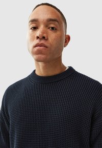 Navy knitted sweater with a ribbed crew neckline and textured pattern. Close-up of the garment, showcasing its thick knit and detailed fabric.