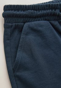 Tengerészkék színű tréningnadrág, rugalmas derékpánttal, oldalzsebbel és puha, texturált anyagból. A varrás részletei jól láthatóak a varrat mentén.