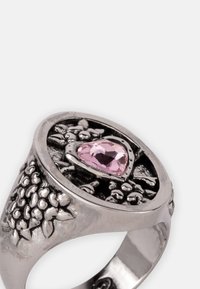 Anillo en tono plateado con una banda texturizada, un diseño floral ornamentado y una piedra preciosa rosa en forma de corazón en el centro.