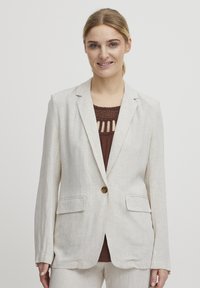 Vaaleanbeige pellavablazeri, jossa on yksi ruskea nappi, kaksi etutaskua, klassiset läpät ja fitted-malli. Sisäpuolella on hienovarainen tekstuuri.