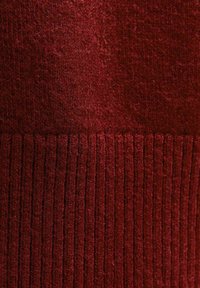 Tissu tricoté en rouge profond avec une section inférieure texturée et côtelée et une section supérieure lisse, mettant en valeur des motifs variés dans le matériau.