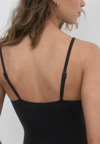 Costume da bagno nero con spalline sottili regolabili, texture liscia e design a schiena bassa. Il tessuto sembra elastico e aderente.