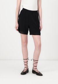 Black shorts with an elastic waistband; scalloped lace detail at the hem. Paired with black flats featuring crisscross straps around the ankles.