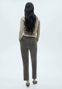 Pull en beige bien ajusté et pantalon tailleur gris, avec un design droit, des poches latérales et une texture lisse. Des escarpins noirs complètent le look.