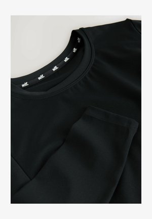 Black long-sleeve shirt with a round neckline, front pocket, and a smooth texture. Label inside collar features the word "self."