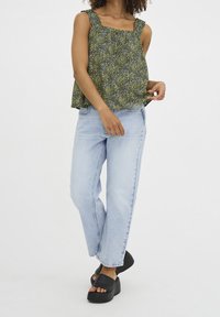 Blommönstrad ärmlös topp i svart och gult, med smockad midja och fyrkantig halsringning. Parat med ljusblå vida jeans och svarta platåsandaler.