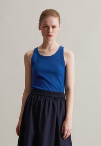 Niebieski prążkowany top na ramiączkach z okrągłym dekoltem, zestawiony z czarną spódnicą z elastycznym paskiem. Materiały wydają się miękkie i lekkie.