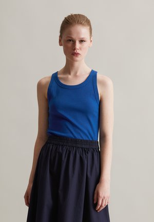 Top in maglia blu con girocollo, abbinato a una gonna nera con una vita elastica. I materiali sembrano morbidi e leggeri.