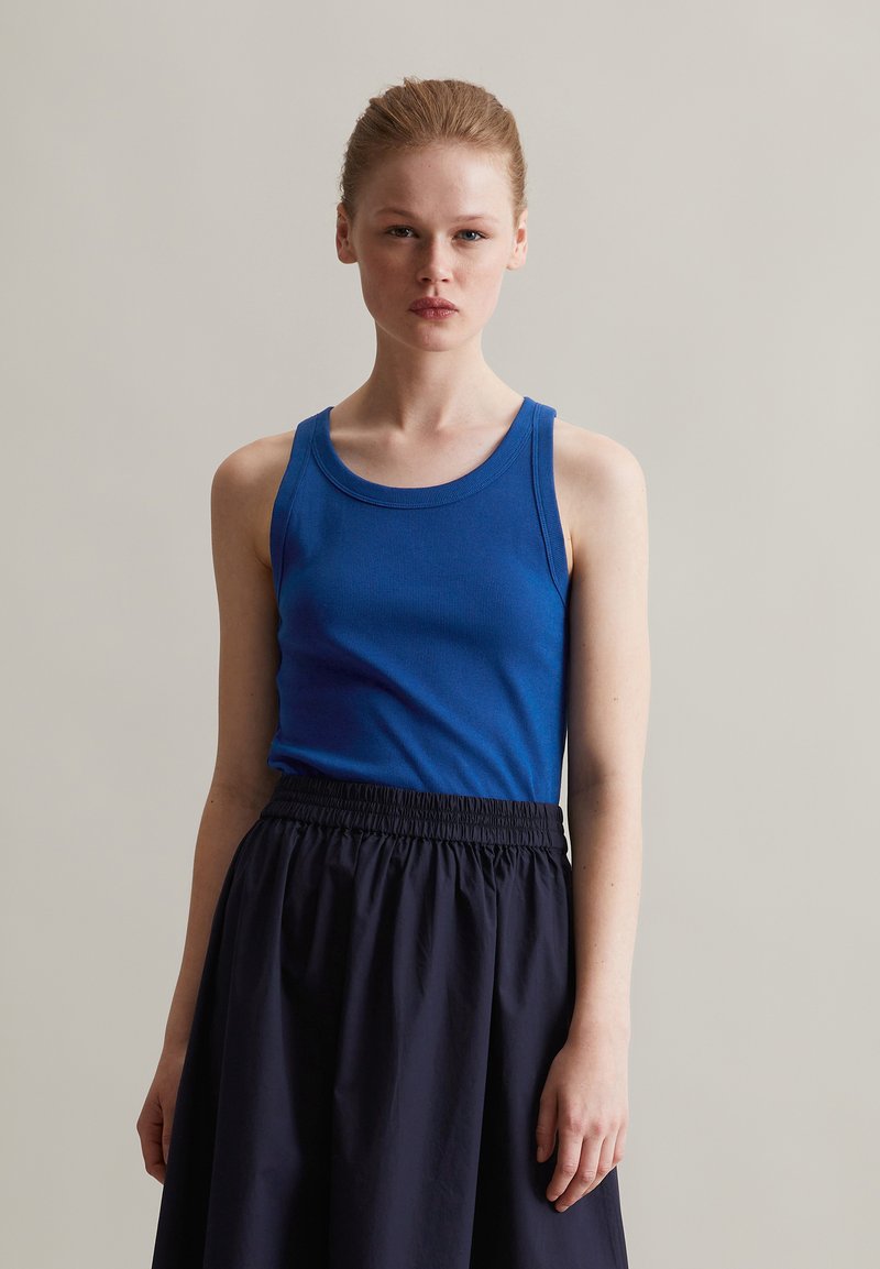 Niebieski prążkowany top na ramiączkach z okrągłym dekoltem, zestawiony z czarną spódnicą z elastycznym paskiem. Materiały wydają się miękkie i lekkie.