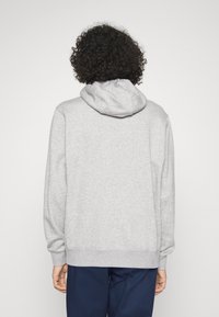 Grå huvtröja med långa ärmar, avslappnad passform, ribbade ärmslut och nederkant, sedd bakifrån mot en enkel bakgrund.