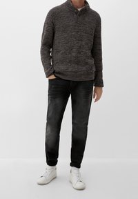 Stickad mörkgrå tröja med hög krage och knapppdetalj, kombinerad med svarta denimjeans och vita sneakers. Avslappnad passform och texturerad finish.