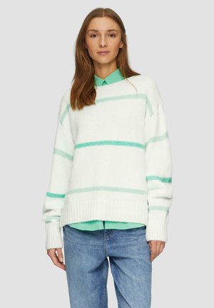 Crèmekleurige trui met mintgroene strepen, geribde manchetten en zoom, gelaagd over een mintgroen overhemd met kraag, gecombineerd met blauwe jeans.