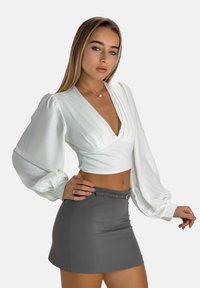 Witte crop top met diepe V-hals en textuur pofmouwen, gecombineerd met een grijze minirok met een tailleriem.