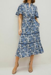 Kukallinen, sinivalkoinen paisley-kuosinen mekko, jossa on lyhyet hihat, vyötärölle solmittava nauha ja levenevä helma. Mekko on valmistettu kevyestä kankaasta ja siinä on taskut.