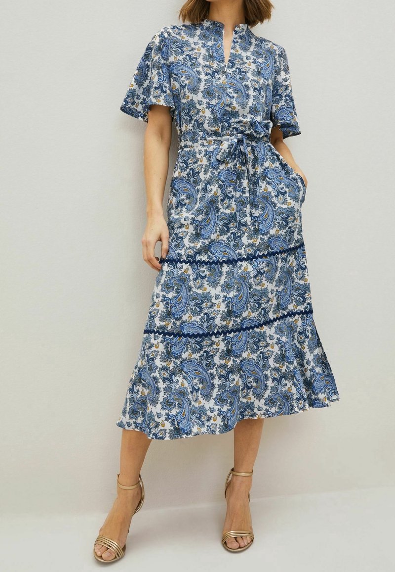 Kukallinen, sinivalkoinen paisley-kuosinen mekko, jossa on lyhyet hihat, vyötärölle solmittava nauha ja levenevä helma. Mekko on valmistettu kevyestä kankaasta ja siinä on taskut.