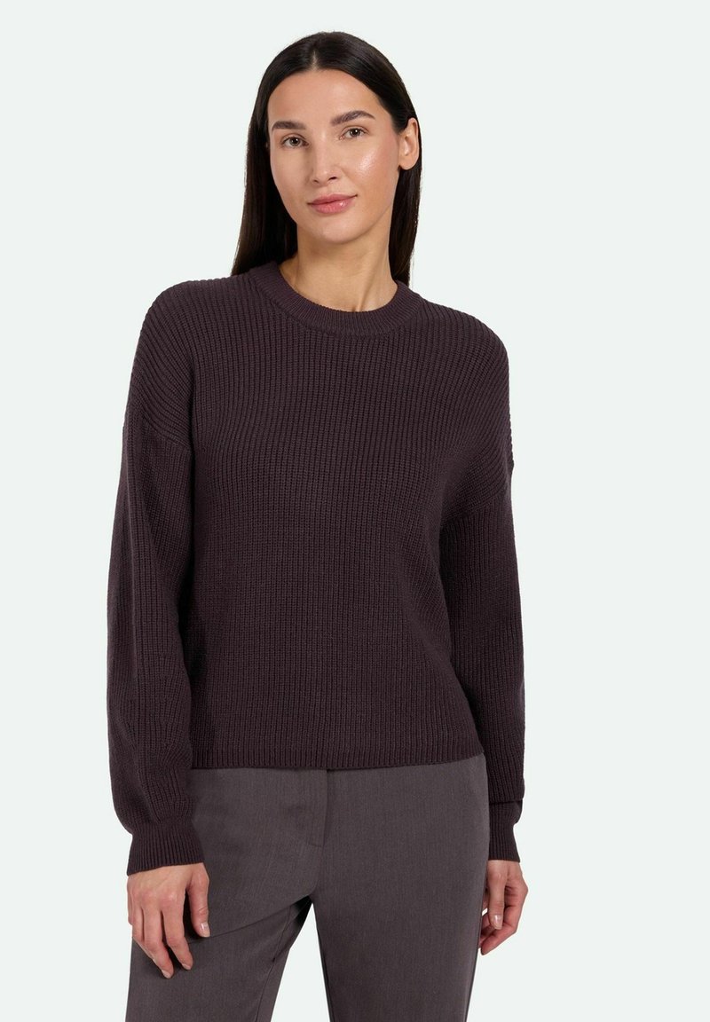 Dark purple knitted sweater with a round neckline, ribbed texture, and long sleeves. Worn with gray pants, showcasing a relaxed fit.