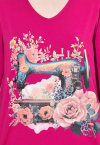 Fuksia T-paita, jossa on vintage-ompelukoneen graafinen kuva, johon on lisätty värikkäitä kukkia, ruusuja ja lehtikoristeita.