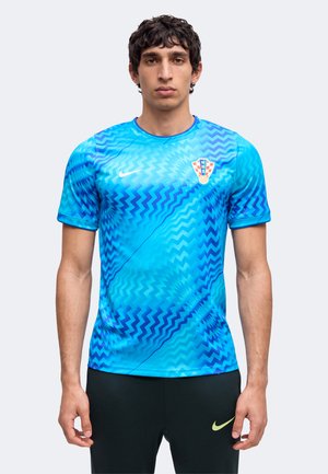 Homme portant un maillot de sport bleu à motif zigzag avec un écusson de football croate et un pantalon noir avec un logo Nike jaune.