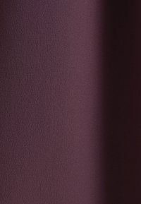 Strukturiertstoff in einem tiefen lila Farbton, mit einem feinen Webmuster. Die Oberfläche wirkt glatt mit einer weichen, einladenden Textur.