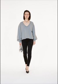Maglione grigio a V oversize, pantaloni neri attillati, tacchi a pois, borsa argentata. Texture liscia; design casual con maniche voluminose.