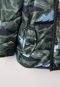 Chaqueta de camuflaje acolchada en tonos verdes y negros, con un patrón de montañas azules, bolsillo lateral abotonado y un acabado texturizado.