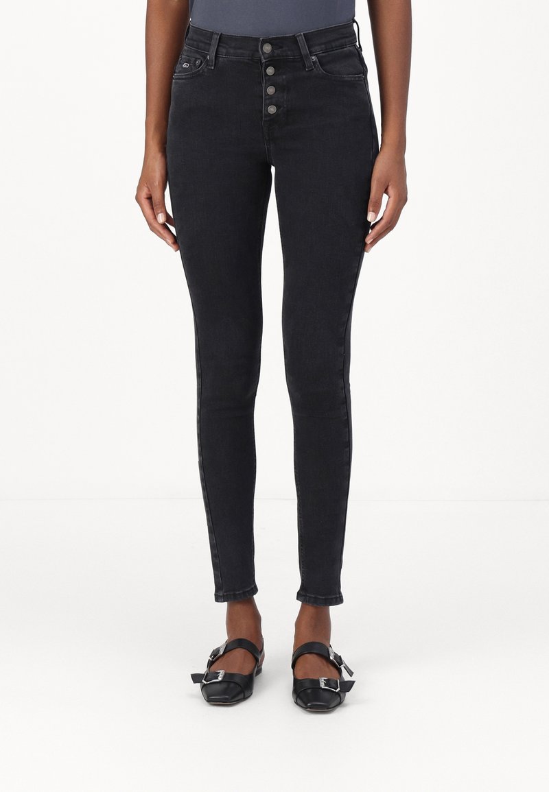 Černé vysoký pas úzké džíny s pěti knoflíkovým zapínáním, předními kapsami a úzkým střihem. Kombinovány s černými botami se čtvercovou špičkou a kotníkovými pásky.