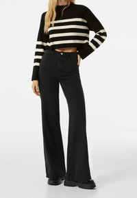 Czarnobiały prążkowany top typu crop z krótkim rękawem, zestawiony z czarnymi, rozszerzanymi jeansami z wysokim stanem. Strój charakteryzuje się dopasowanym krojem i teksturowaną tkaniną.