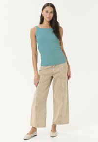 Débardeur bleu-vert clair avec une texture côtelée, associé à un pantalon large beige avec des coutures contrastantes et une finition lisse.