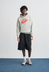 Γκρι φούτερ με κουκούλα και κόκκινο λογότυπο «Just Do It», μαύρο σορτς και γκρι αθλητικά παπούτσια. Διαθέτει τσέπη καγκουρό και ριμπ μανσέτες. Απλός σχεδιασμός.