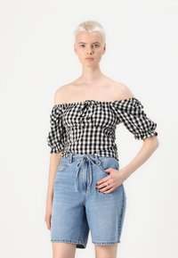 Black and white gingham off-shoulder top with puffed sleeves and a tied front, paired with high-waisted light blue denim shorts.
