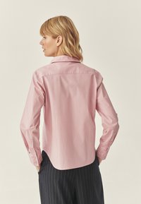 Jasnoróżowa koszula z długim rękawem i klasycznym kołnierzykiem, z zapięciem na guziki przy mankietach oraz zaokrąglonym dołem, wykonana z gładkiego materiału bawełnianego.