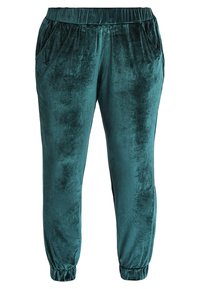 Jogging en velours teal avec une taille élastique, des poches latérales et des poignets froncés. Texture douce avec une finition lisse et un léger éclat.