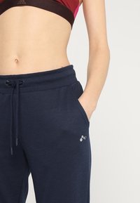 Marina blå sweatpants i mjukt tyg, med dragsko i midjan, sidofickor och en liten logodetalj på vänstra låret.