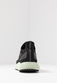 Zapatilla deportiva negra con parte superior de punto transpirable, panel trasero texturizado y una única suela media de rejilla verde con suela negra.