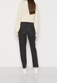 Svarta denimjeans med rak passform och två bakfickor, tillsammans med en krämfärgad stickad tröja med ribbade detaljer.