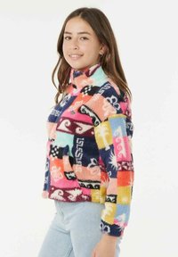 Fleece-pullover med høj krave, der har et flerfarvet patchworkdesign i pink, blå og gul med abstrakte mønstre.