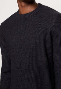 Dark gray knit sweater with a textured surface, round neckline, and ribbed cuffs. Fabric appears warm and slightly thick for added comfort.