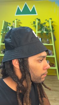 Black bucket hat with a wide brim, fabric loops, and chin strap. Features a stitched logo on the front. Textured surface and simple design.