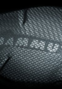 Svart mesh-stoff med et bikakesymønster og en subtil vertikal stripe som viser teksten "AMRU." Teksturen virker jevn.
