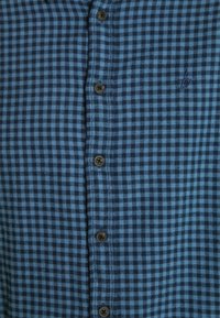 Blauw en zwart geruit overhemdd met bruine knopen en een klein geborduurd logo aan de linkerkant. Zachte katoenen stof.