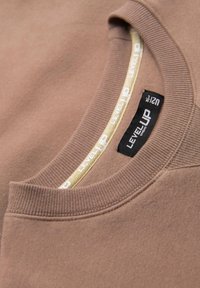 Brauner Sweater mit geripptem Rundhalsausschnitt, der ein strukturiertes Innenetikett und kontrastierende weiße und gelbe Akzente entlang des Ausschnitts aufweist.