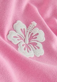 Tissu de pull rose avec un motif de fleur d'hibiscus blanche, présentant des coutures texturées et une surface lisse.